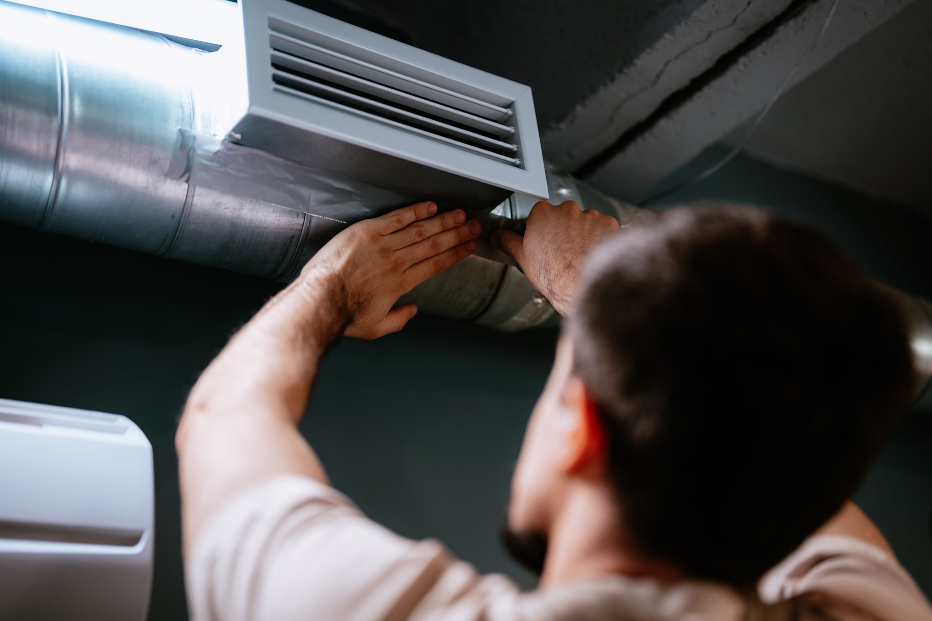 Technician repairing air duct in industrial space during daytime while focused on maintenance task